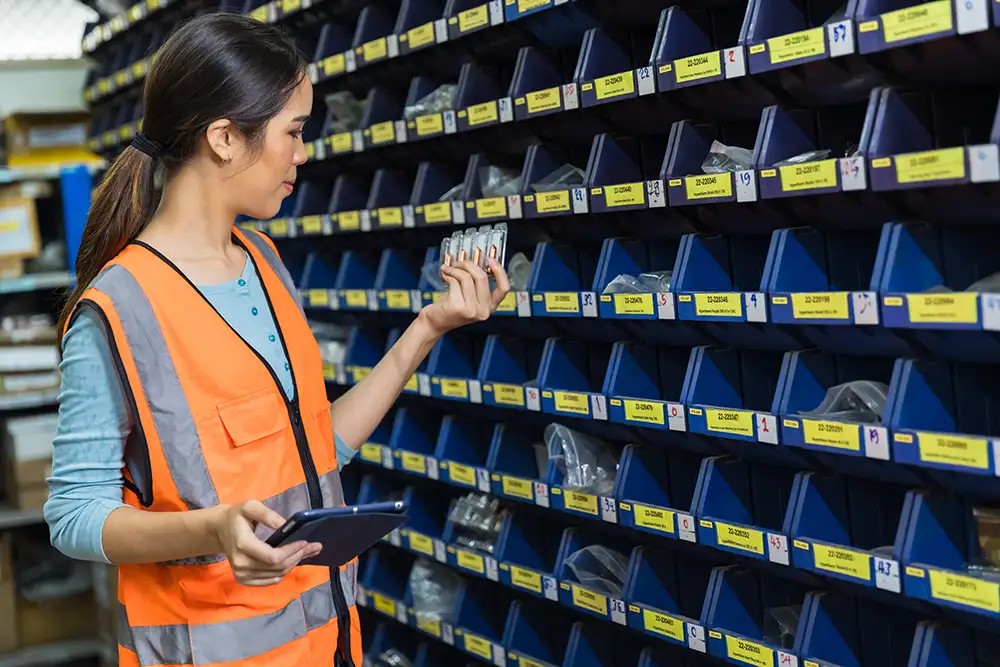 Warehouse worker with tablet checking labeled parts bins for vendor management workflow